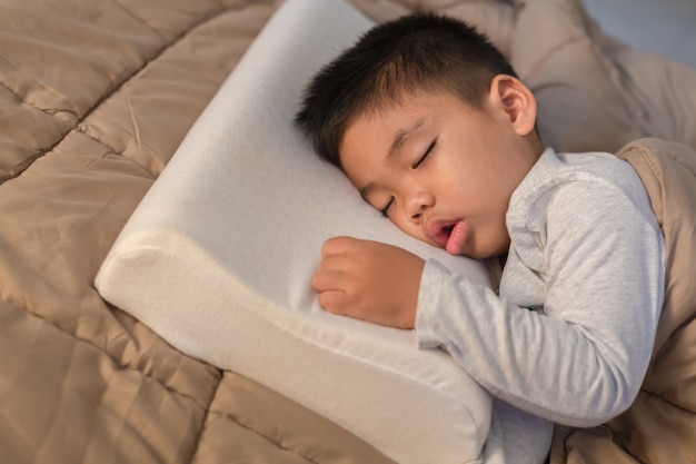 Asian little boy Sleeping on a warm brown fabric on the bed, happily