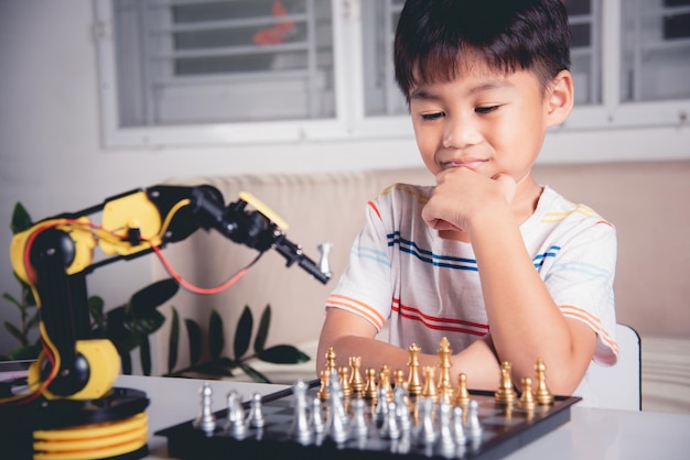 Asian little boy thinking and wait robot arm playing chess