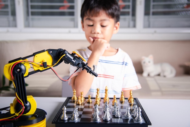 Asian little boy thinking and wait robot arm playing chess