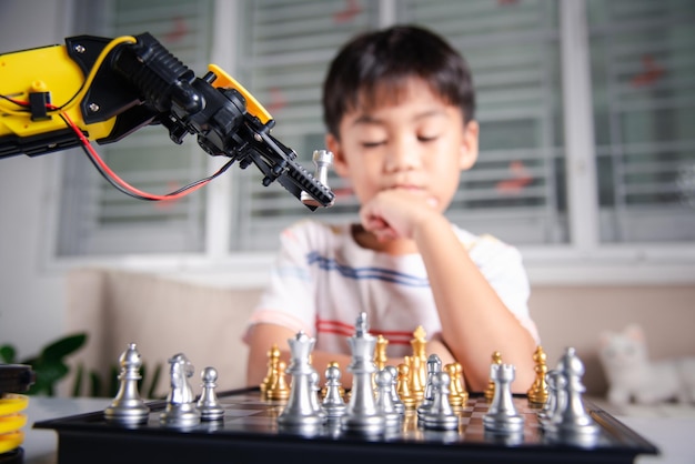 Asian little boy thinking and wait robot arm playing chess