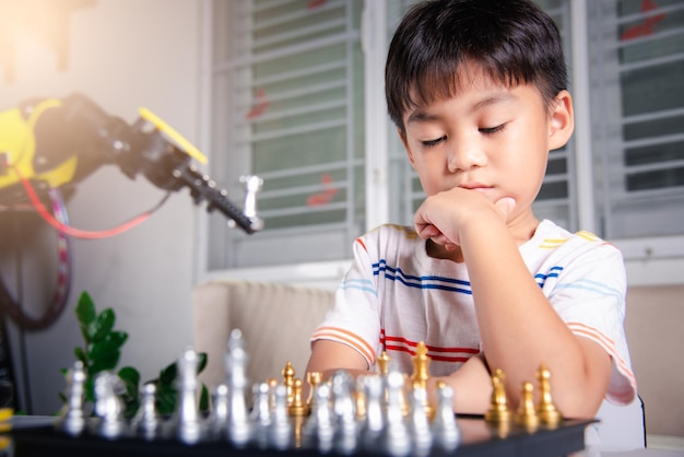 Asian little boy thinking and wait robot arm playing chess