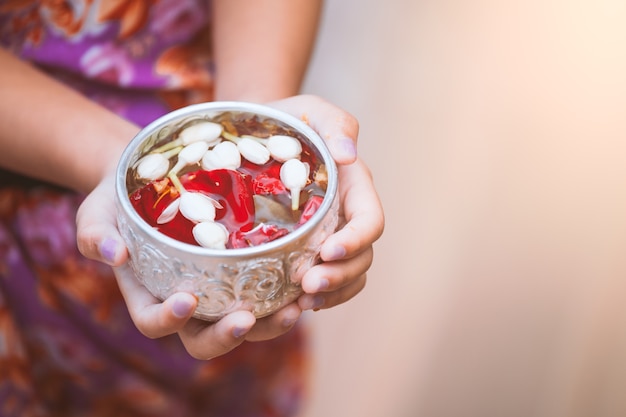 Asian little child girl holding bowl that have flower leaf in water for pouring on hands o