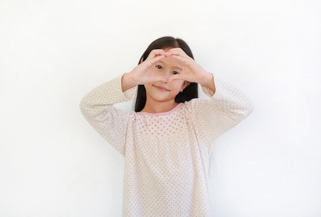 Asian little child girl making fingers for heart sign on eyes on white background Focus at his finger