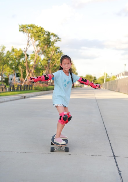 Asian little girl child skateboarder wearing safety and protective equipment playing on skateboard Kid skateboarding on the road outdoors