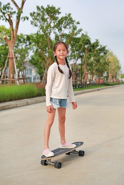 Asian little girl child skating on a skateboard. Kid riding on skateboard outdoors at the street. She skateboarding on the road