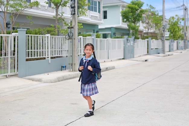 Asian little girl in school uniform wearing a medical mask walking on the street