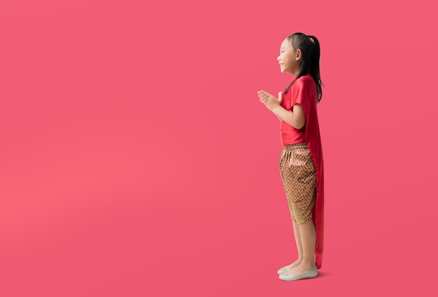 Asian little girl in Thai national costumes with welcome gesture of hands of Thailand isolated on red background with Clipping paths for design work empty free space