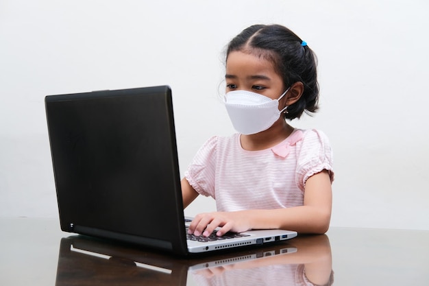 Asian little girl wearing medical mask joining online school from home