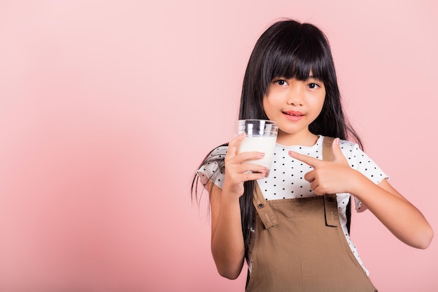 Asian little kid 10 years old smile hold milk glass drink white milk and pointing finger