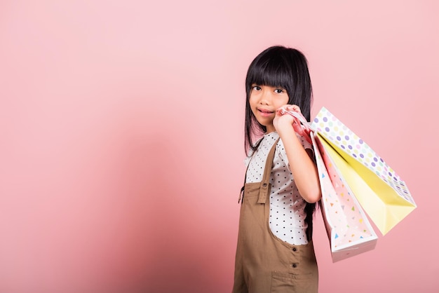 Asian little kid 10 years old smiling holding multicolor shopping bags in hands