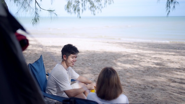 Asian love couple camping on the summer beach. Man playing Ukuleleand together with woman sitting outside the tent.