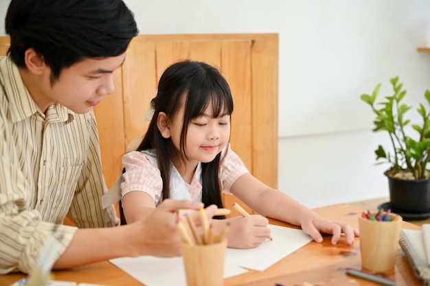 Asian male art teacher teaching a cute young girl student to draw and paint with watercolor