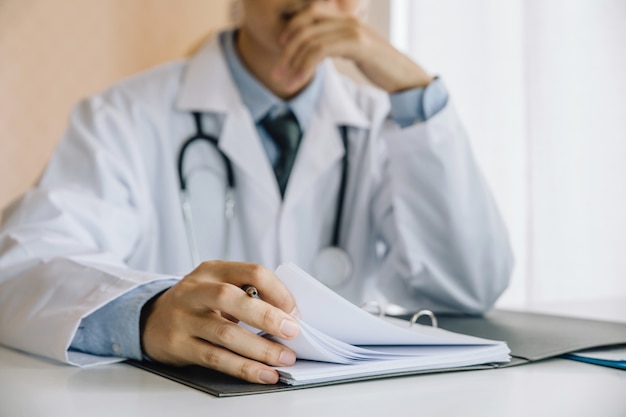 Asian male doctor sitting and hence to rest the chin on his hands and analyzes patient data. 