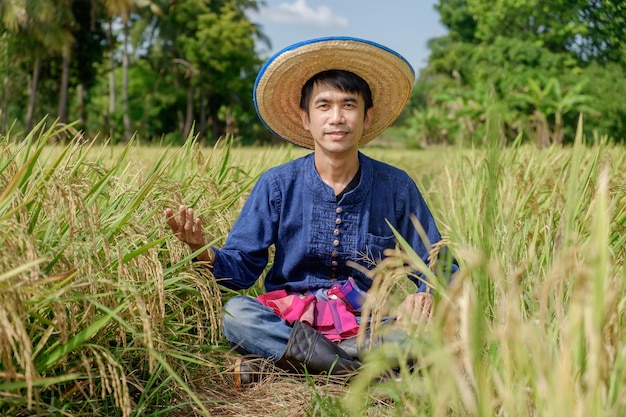 Asian male farmer wearing traditional blue dress Sitting raising his hands with a smiling face in the middle of the field