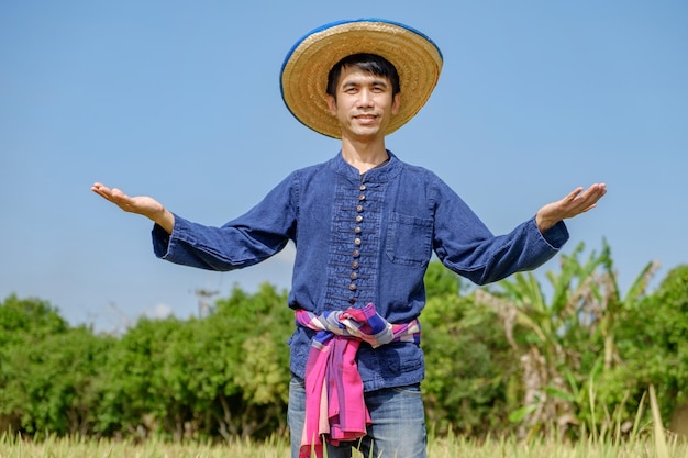 Asian male farmer wearing traditional blue dress standing raising his hands with a smiling face in sky background