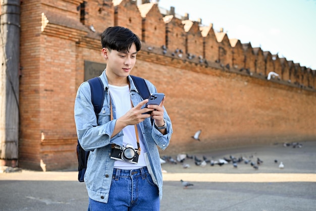 Asian male traveler using his smartphone while strolling at ThaPhae gate or Chiangmai old city