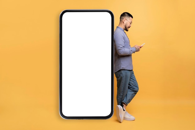 Asian man browsing smartphone and leaning at big blank mobile phone