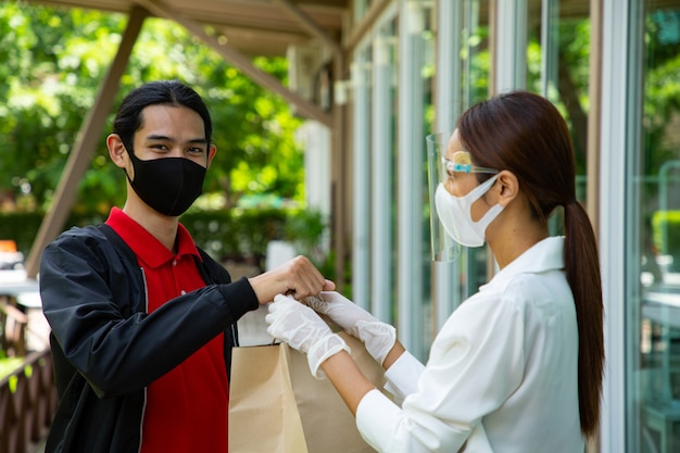 Asian man come to take away food .Delivery man pick up breads from restaurant . Waitress hold food to customer.New Normal customer with mask come to take away food.