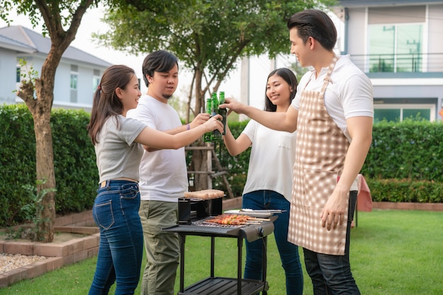 Asian man cooking barbeque grill and sausage for a group of friends to eat party in garden at home.