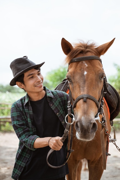 Asian man in cowboy hat leads the horses head on the leash at the ranch