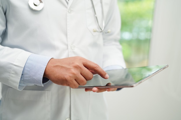 Asian man doctor using tablet computer to reading patient report check up and search for solve treatment health medical online in hospital