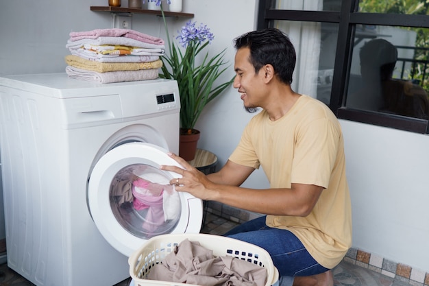 asian Man doing laundry at home loading clothes into washing machine