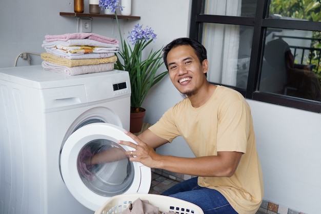 asian Man doing laundry at home loading clothes into washing machine