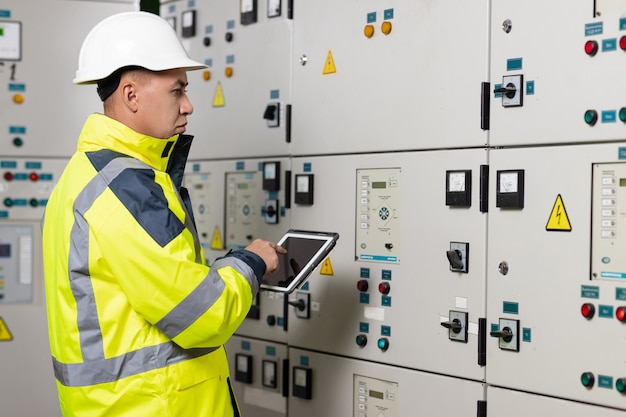 Asian man electrical engineer hold tablet monitoring electrical system in control room technician