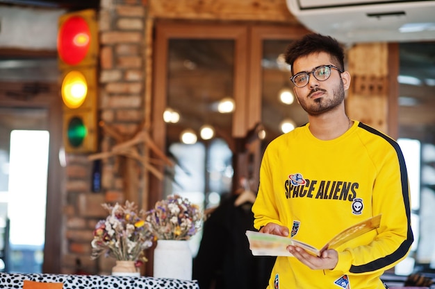 Asian man in eyewear and yellow sweatshirt posing indoor cafe with traffic light