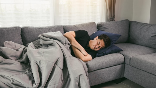 Asian man feel the illness while he was cold lying on the sofa and wearing a blanket at his house