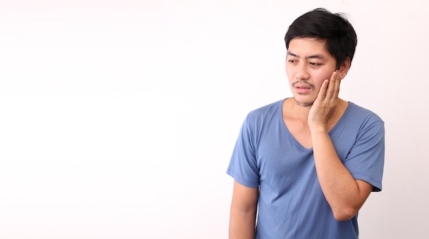 Asian man feeling pain, holding his cheek with hand, suffering from bad tooth ache.