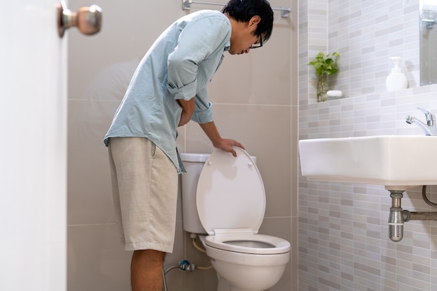 An Asian man in front of the toilet has severe abdominal pain.