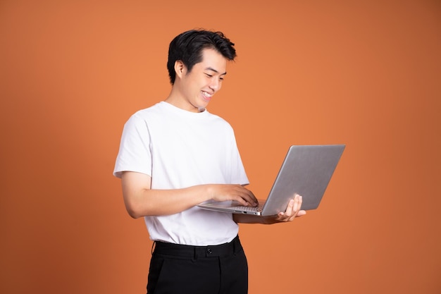 Asian man holding laptop isolated on orange background