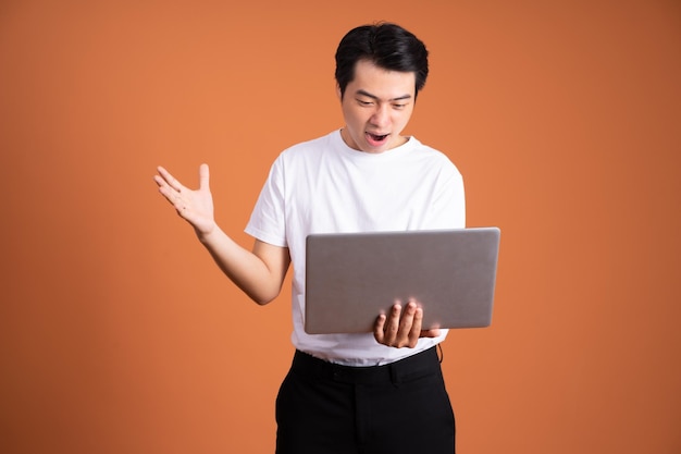 Asian man holding laptop isolated on orange background