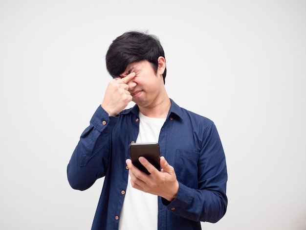 Asian man holding mobile phone and feeling tried his eyes white background