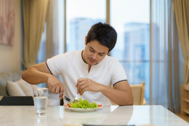 An Asian man is eating an American breakfast in the living room at home.
