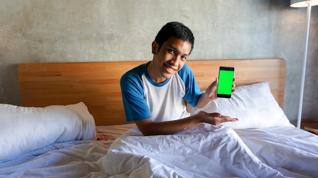 Asian man is holding a green screen handphone in the bedroom