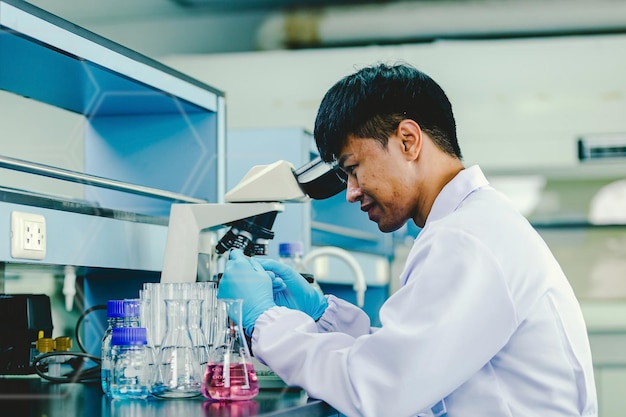 Asian man lab technician in protective glasses and gloves sits next to a microscope in laboratory