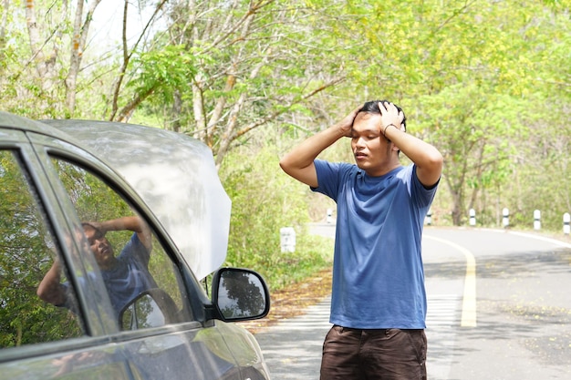 Asian man looks at broken car engine while traveling