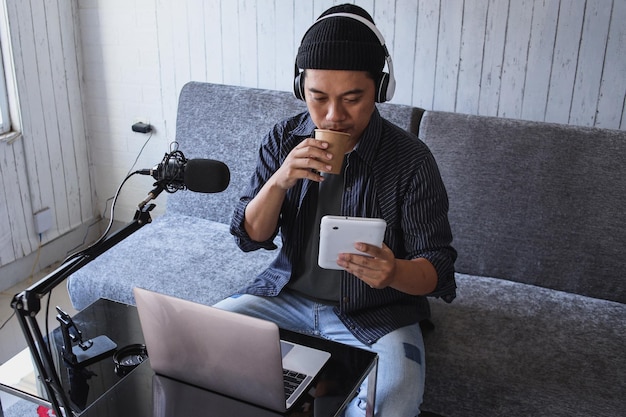 Asian man making a podcast from home studio while holding mobile phone. Recording a podcast for onli