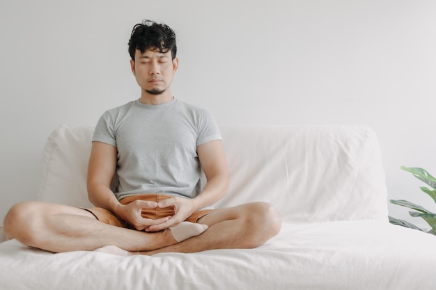 Asian man do meditation on the sofa in his apartment