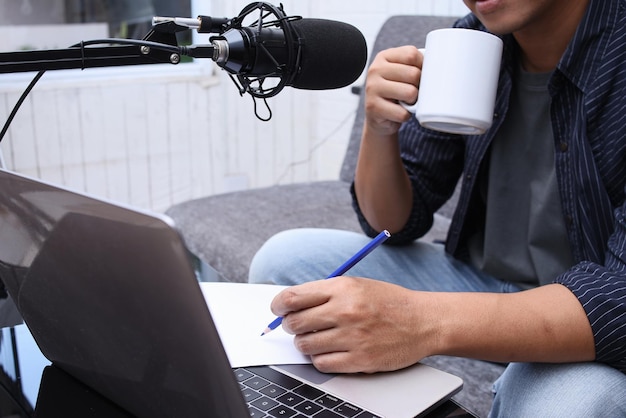 Asian man radio program host recording audio podcast using professional equipment while making notes