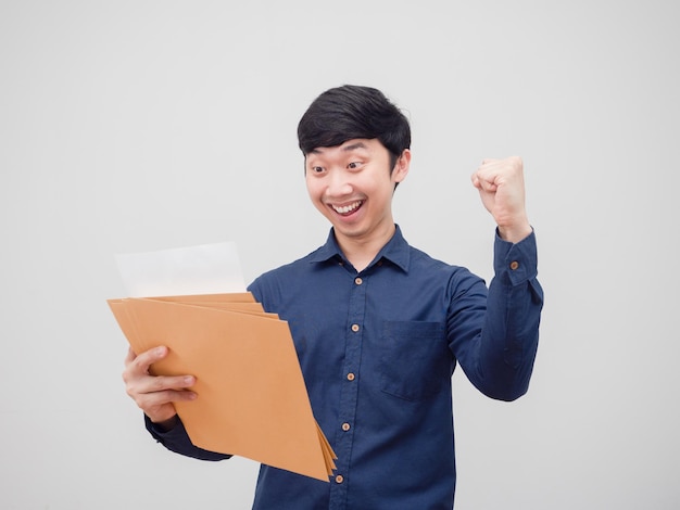 Asian man reading at document envelope in hand feeling happy and smile show fist up white background