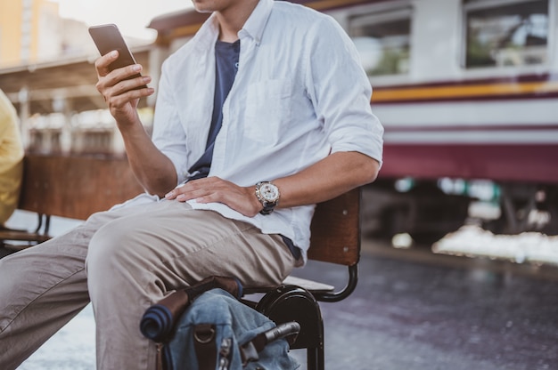 Asian man returning from a vacation on a train journey, and he is using a smartphone to pick up his relatives at the station.Holiday, journey, trip and summer Travel concept.