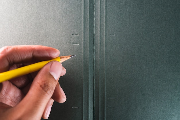 Asian man's hand hold a yellow pencil on dark green paper