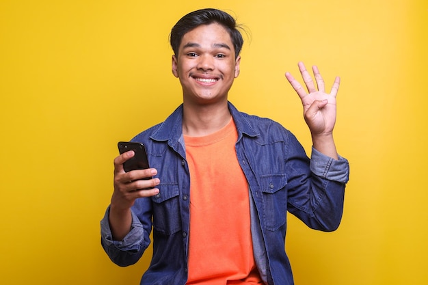 Asian man showing fingers number four while smiling and holding smartphone