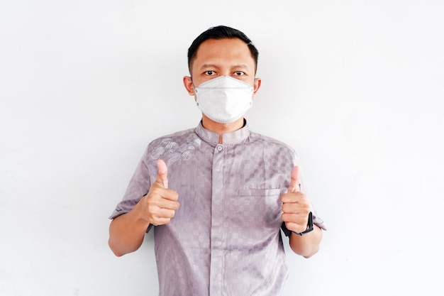 Asian man shows how to wear a mask and gives two thumb gesture isolated on white background.