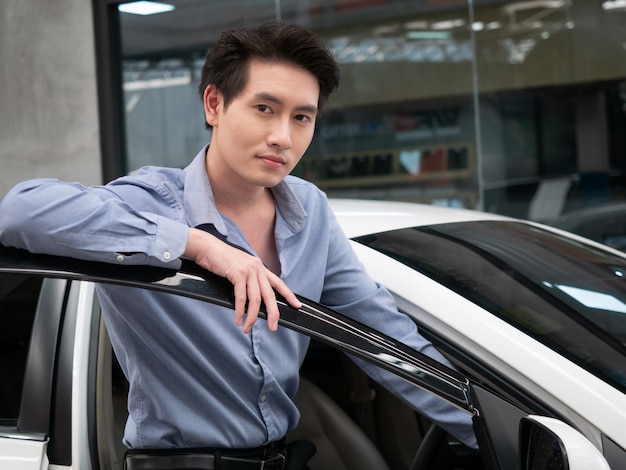 Asian man sitting in new car and showing car keys. Young attractive man sitting salon automobile looking out open window.