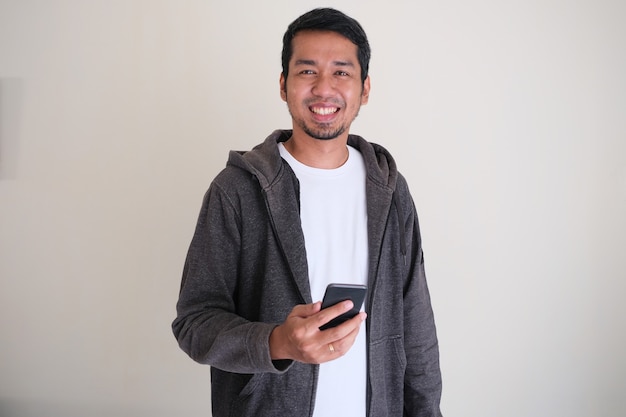 Asian man standing confident and smiling while holding a mobile phone