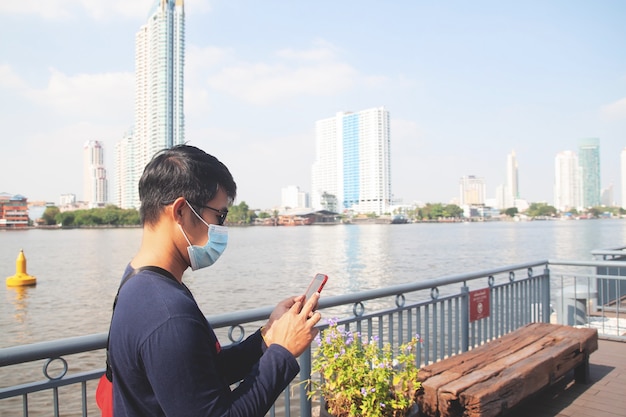 Asian man tourist wearing face mask using mobile phone at Bangkok travel location